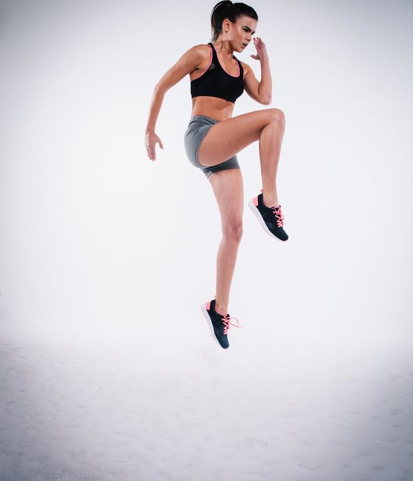 Woman in activewear performing a light cardio movement in a minimalist dark studio.